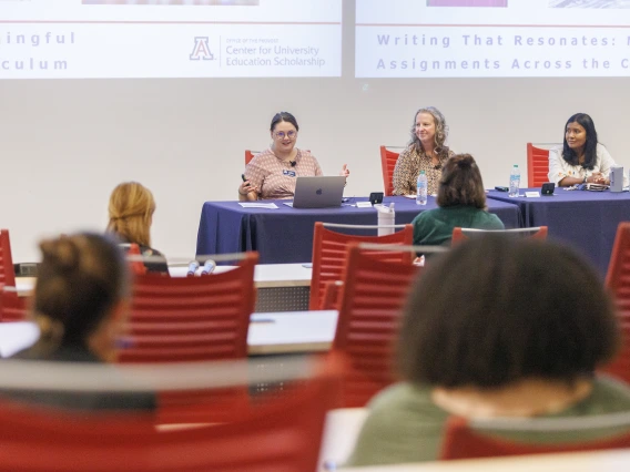 Three women sit at a panel table during a University of Arizona presentation on writing assignments.