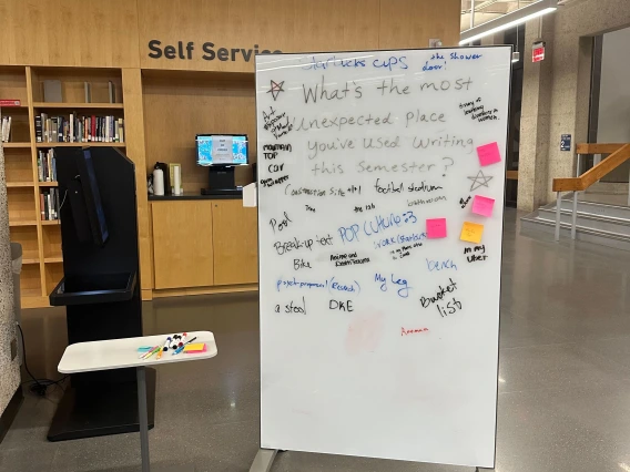 A whiteboard in a "Self Service" area of the Main Library (2nd floor) filled with handwritten responses to the prompt: "What's the most unexpected place you've used writing this Semester?"